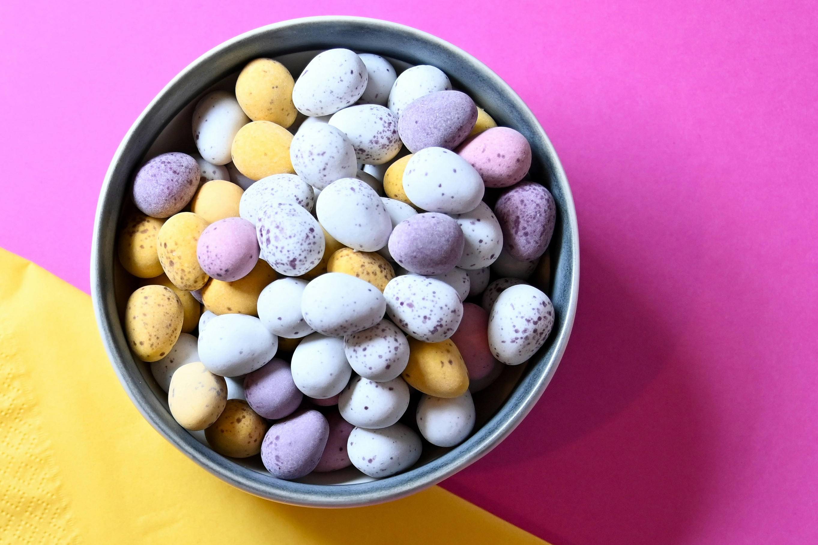 Pastel Mini Eggs in a bowl on a bright pink and yellow background.